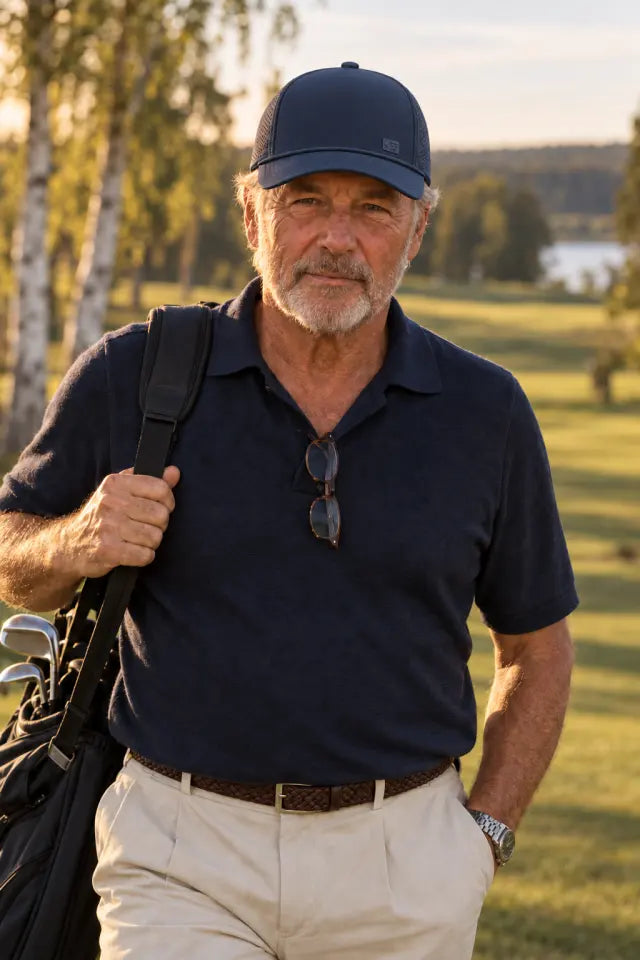 Older man in a navy knitted golf polo on the fairway in evening sun, navy cap with a small silicone patch bearing the symbol